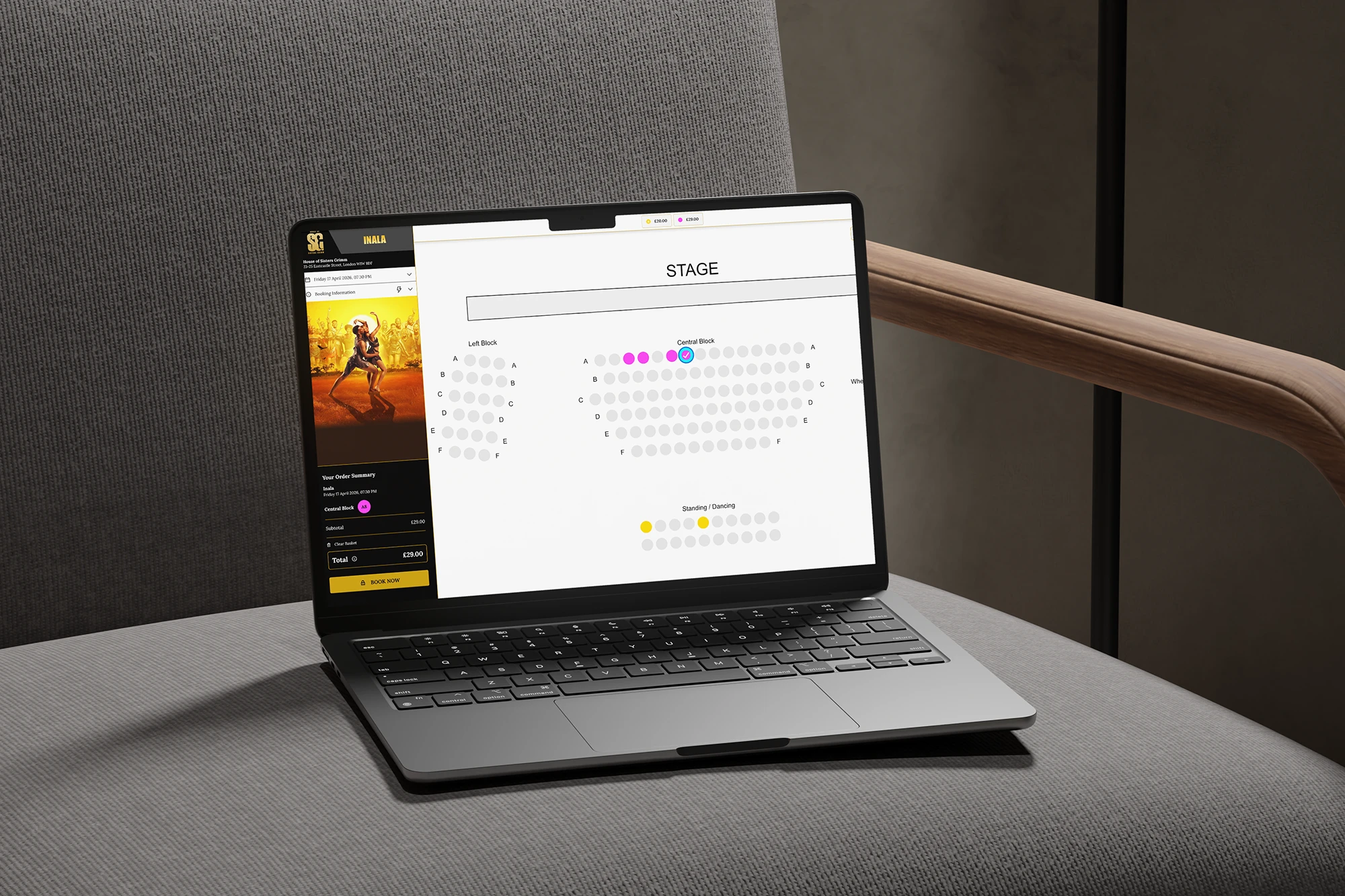 Laptop displaying a theatre seating chart on a grey sofa with a wooden armrest.