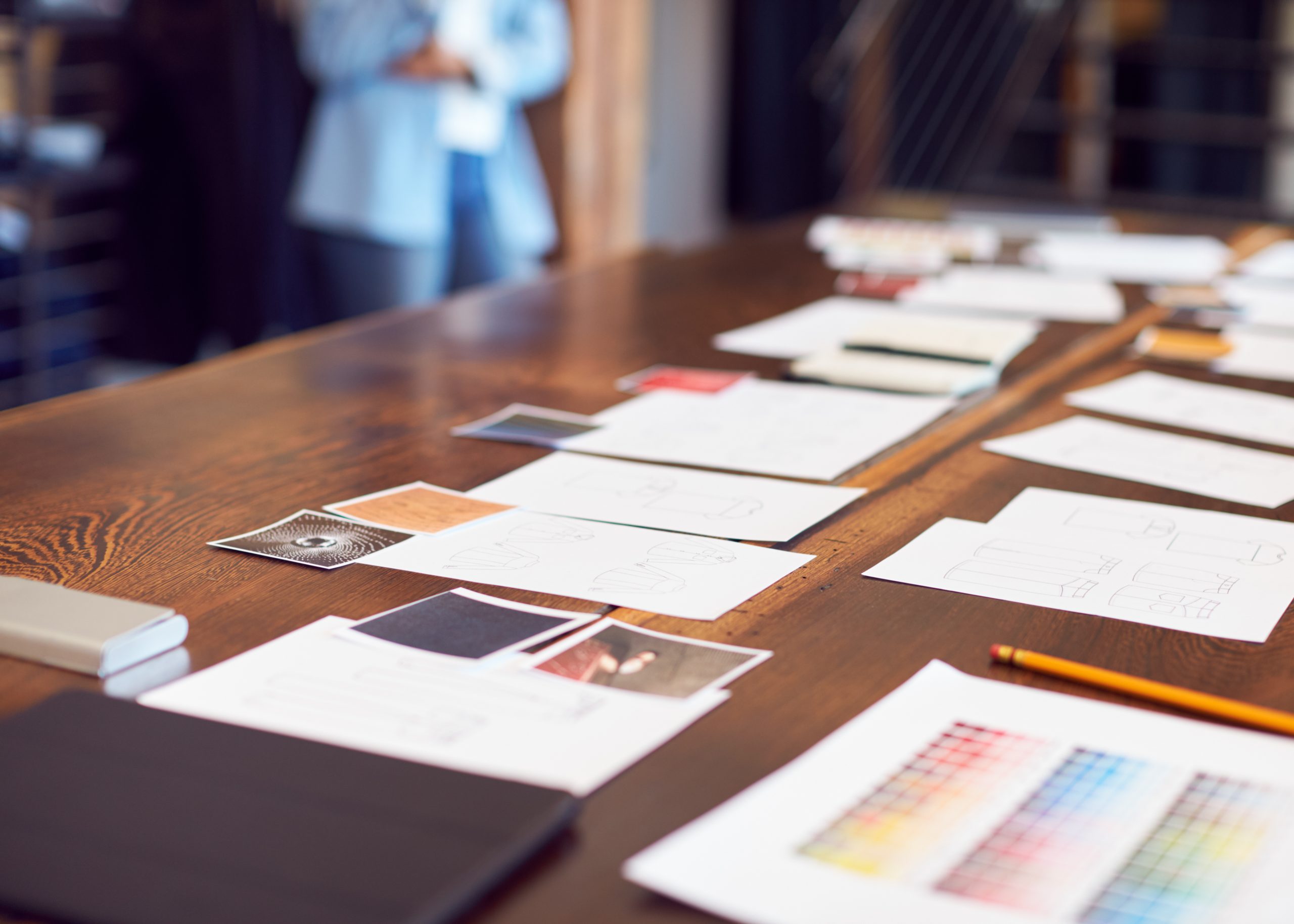 Creative workspace with sketches, colour palettes, and design plans on a wooden table.