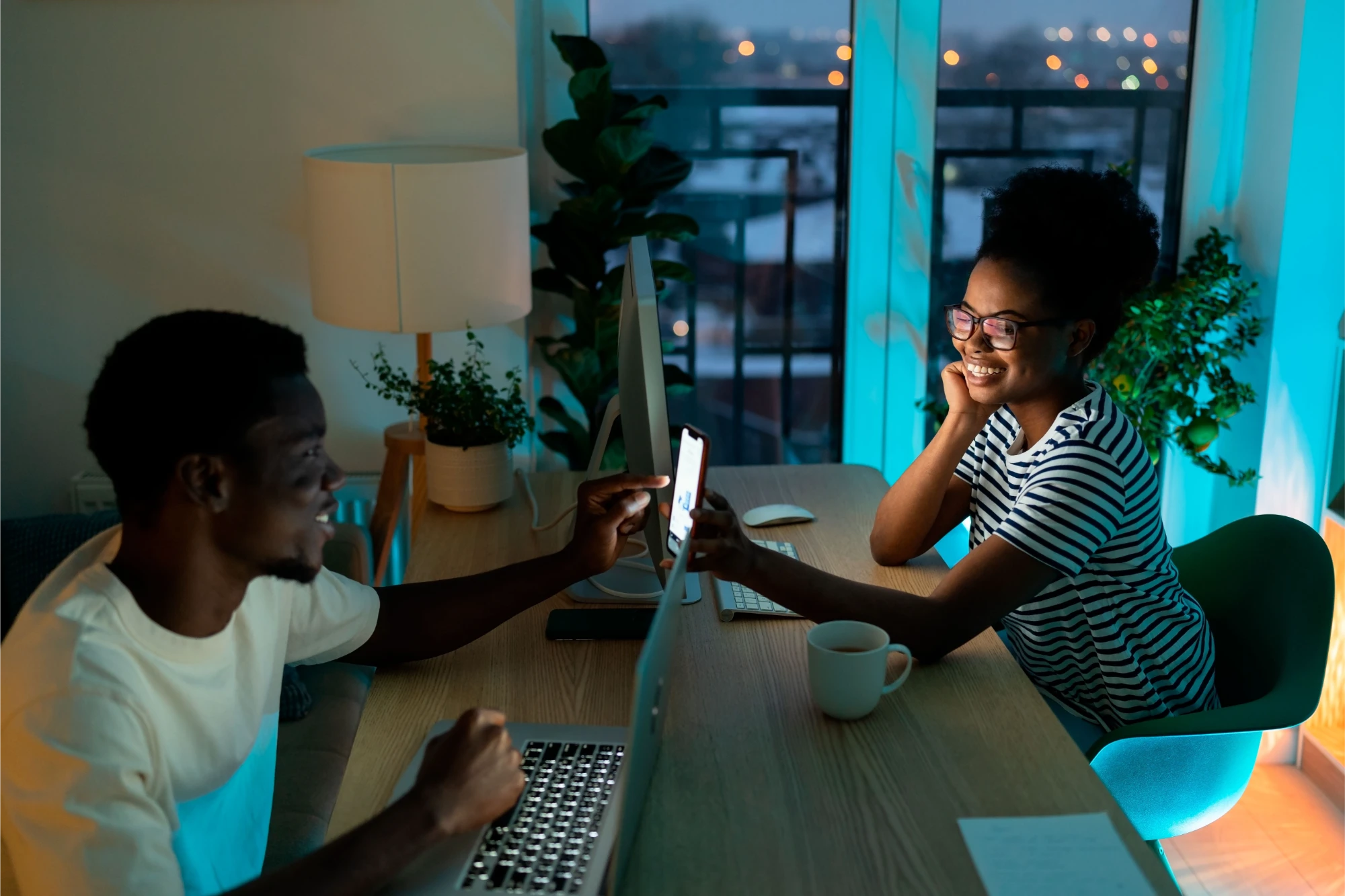 Two diverse women working together at a desk with computers and a window view.
